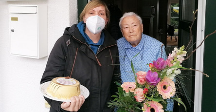 Einrichtungsleiterin gratuliert Mieterin mit Kuchen und Blumen