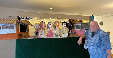 Ein Bewohner des ProCurand Pflegestifts Pfarrer Lukas in Cham steht an einer Werkbank, auf der mehrere selbst gebastelte Handpuppen arrangiert sind.