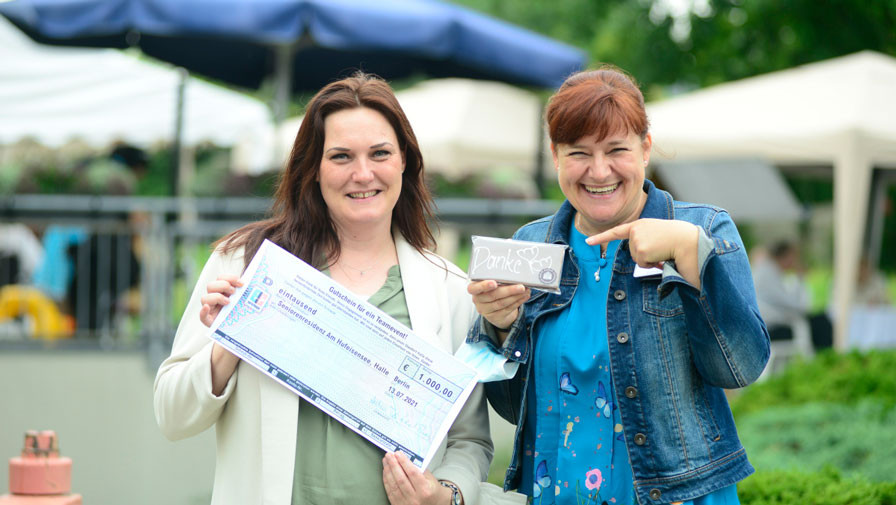 ProCurand Einrichtungsleiterin und Pflegedienstleiterin mit einem Gutschein für ein Teamevent vor der Seniorenresidenz Am Hufeisensee