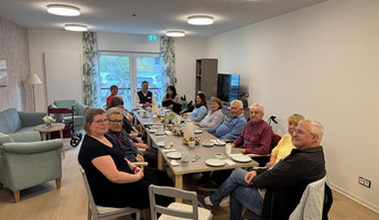 In der ProCurand Wohngemeinschaft Residenz Nordend sitzen die WG-Mitglieder mit Angehörigen gemütlich beisammen und tauschen sich beim gemeinsamen Essen über das zukünftige Zusammenleben aus.