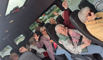 Die Gäste der ProCurand Tagespflege Strausberg sitzen gut gelaunt im Kleinbus nach Oderberg, lachen und heben voller Freude die Hände in die Luft.