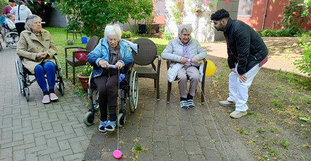 Im Garten der ProCurand Seniorenresidenz Havelpalais ziehen zwei Seniorinnen beim Spiel „Enten aufwickeln“ mit viel Geschick die Bälle an einem Seil zu sich.