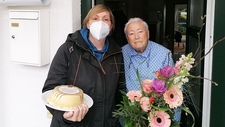 Einrichtungsleiterin gratuliert Mieterin mit Kuchen und Blumen
