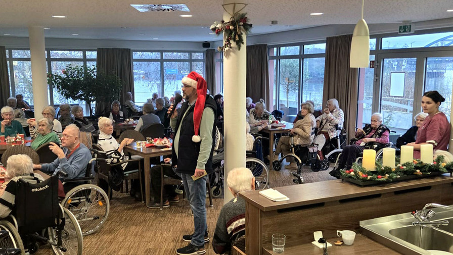Bewohner*innen sitzen im Café Havelterrasse der ProCurand Seniorenresidenz Havelpalais an weihnachtlich gedeckten Tischen, während eine als Weihnachtsmann verkleidete Person durch den Raum geht.