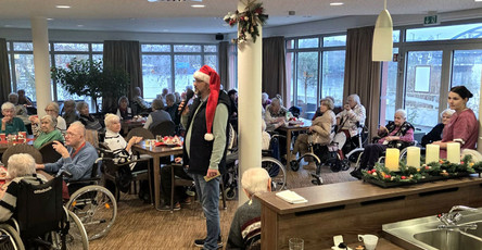 Bewohner*innen sitzen im Café Havelterrasse der ProCurand Seniorenresidenz Havelpalais an weihnachtlich gedeckten Tischen, während eine als Weihnachtsmann verkleidete Person durch den Raum geht.