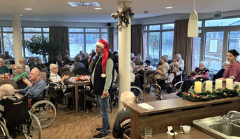 Bewohner*innen sitzen im Café Havelterrasse der ProCurand Seniorenresidenz Havelpalais an weihnachtlich gedeckten Tischen, während eine als Weihnachtsmann verkleidete Person durch den Raum geht.