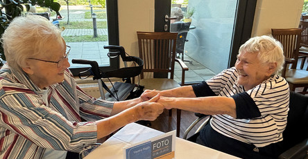 Zwei Seniorinnen der ProCurand Seniorenresidenz Bölschestraße halten sich an den Händen und haben beim Tanztee sichtbar Freude.