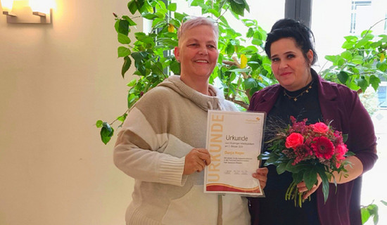 In der ProCurand Seniorenresidenz Park Sanssouci überreicht Pflegedienstleitung Manuela Grund ihrer Kollegin Dunja Hoyer zum 20-jährigen Dienstjubiläum eine Urkunde und einen Blumenstrauß.