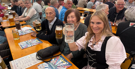 Die Bewohner*innen und eine Mitarbeiterin des ProCurand Pflegestifts Pfarrer Lukas sitzen am Tisch zusammen, lachen und stoßen gemeinsam mit Bierkrügen auf einen fröhlichen Nachmittag beim Chamer Volksfest an.
