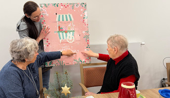In der ProCurand Tagespflege Eberswalde öffnen Gäste gemeinsam mit einer Mitarbeiterin den Adventskalender am festlich dekorierten Tisch.
