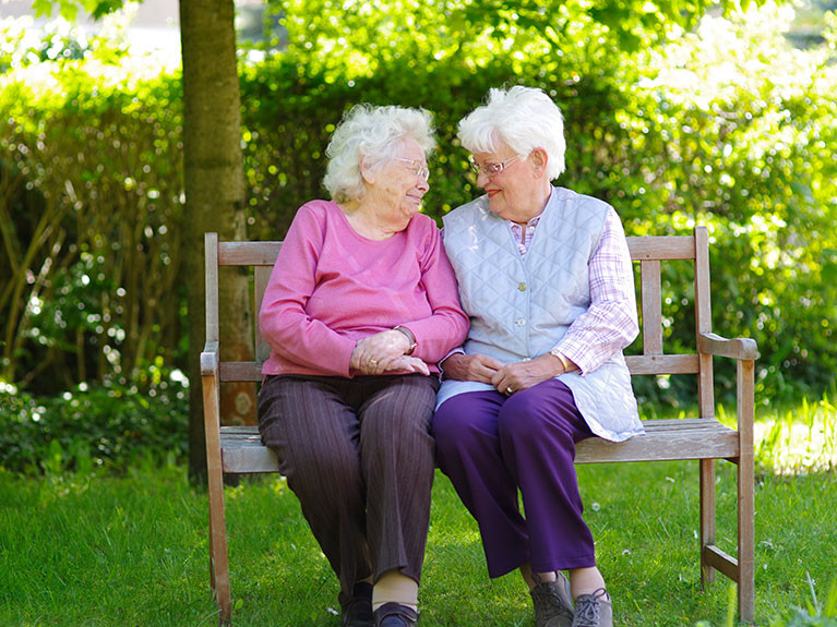 Seniorinnen des Seniorenstifts Neuenhagen-Hauptsraße sitzen gemeinsam auf einer Bank im Garten