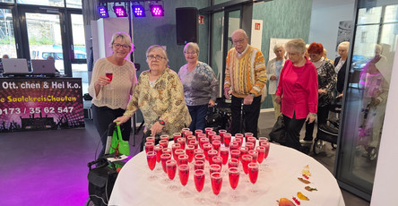 In der ProCurand Seniorenresidenz Am Hallorenring feiern Bewohner*innen zusammen mit der Residenzleitung Melanie End fröhlich zusammen, umgeben von bunter Beleuchtung und festlicher Stimmung.