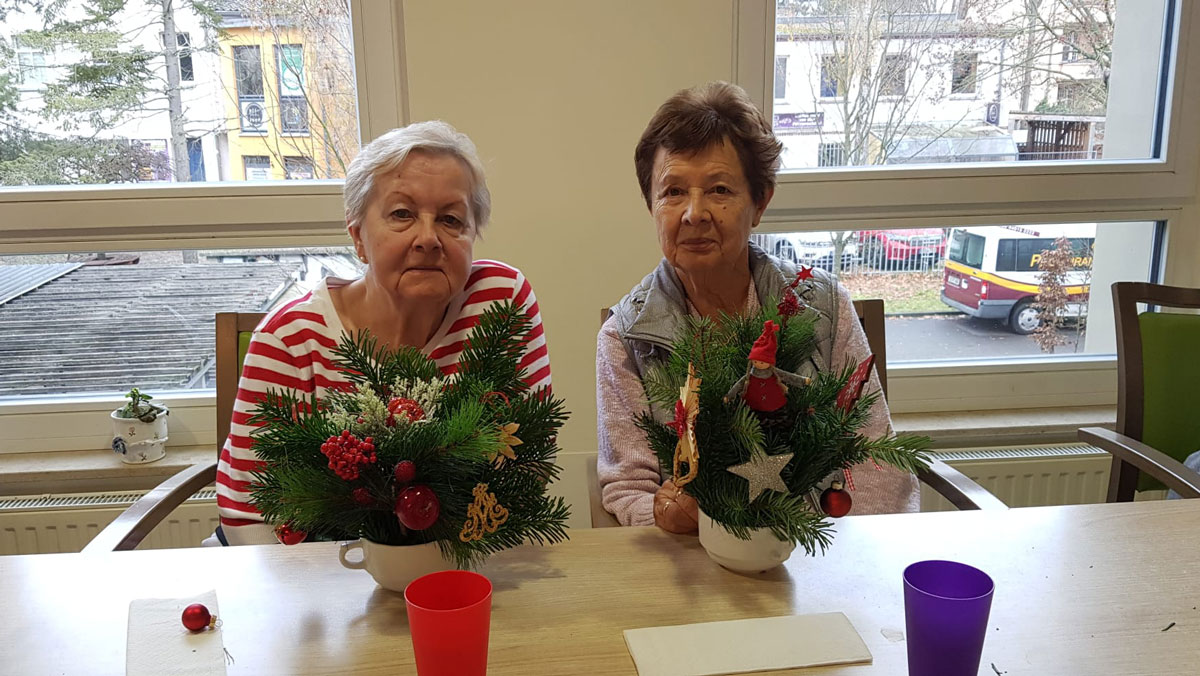 In der ProCurand Seniorenresidenz Bölschestraße sitzen zwei Bewohnerinnen an einem Tisch und gestalten gemeinsam weihnachtliche Adventsdekoration.