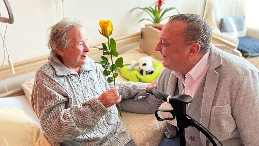 Einrichtungsleiter Matthias Küßner schenkt einer Bewohnerin der ProCurand Seniorenresidenz Bölschestraße eine Rose zum Frauentag.