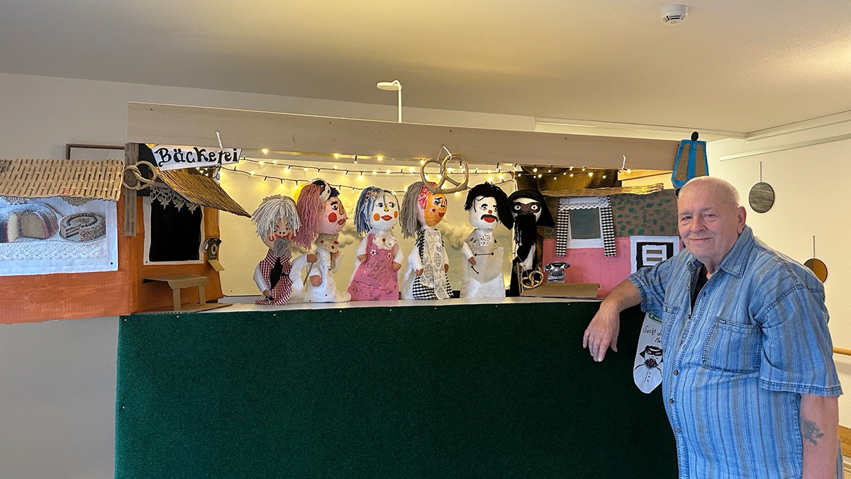 Ein Bewohner des ProCurand Pflegestifts Pfarrer Lukas in Cham steht an einer Werkbank, auf der mehrere selbst gebastelte Handpuppen arrangiert sind.