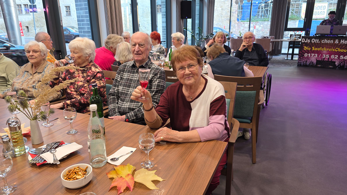 Bewohner*innen der ProCurand Seniorenresidenz Am Hallorenring sitzen gemütlich beisammen, genießen Speisen und Getränke und verbringen einen geselligen Herbstnachmittag.