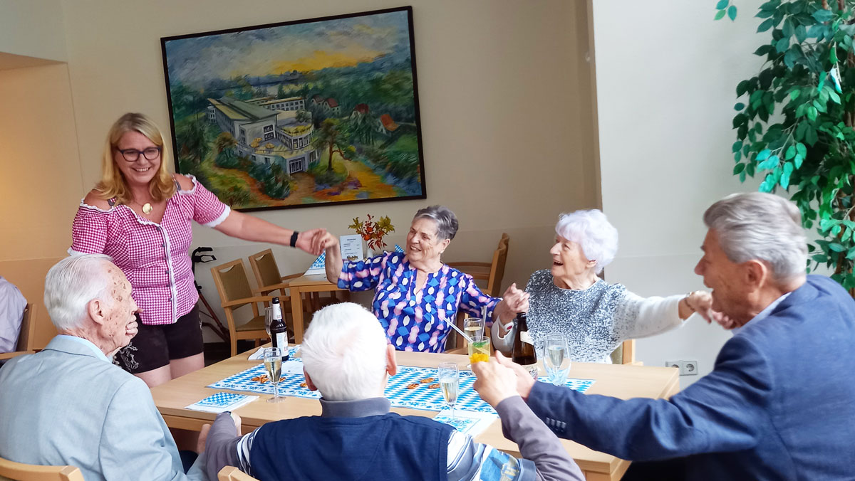 In der ProCurand Seniorenresidenz Am Straussee sitzen Bewohner*innen gemütlich zusammen, unterhalten sich und genießen Getränke, begleitet von herzlicher Betreuung und fröhlicher Stimmung.