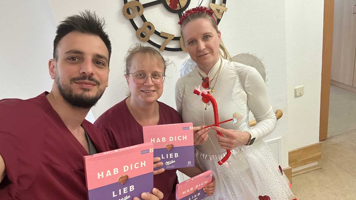 rei Personen halten kleine Aufmerksamkeiten mit liebevollen Botschaften in den H&auml;nden und l&auml;cheln gemeinsam in die Kamera.