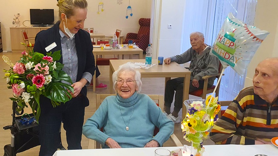 Einrichtungsleitung &uuml;berreicht Seniorin zum 100-j&auml;hrigen Geburtstag einen Blumenstrau&szlig; im Seniorenstift Neuenhagen-Hauptstra&szlig;e