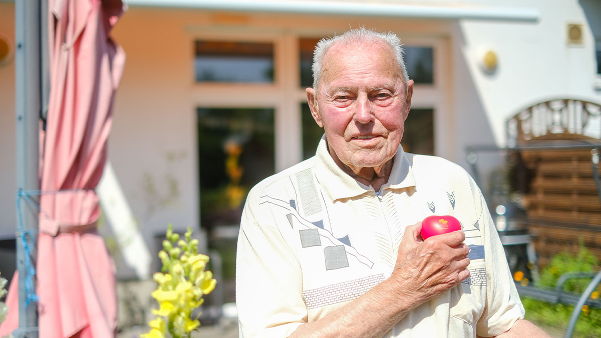 Ein Senior zeigt das ProCurand-Herz im Garten der Tagespflege Nächst-Neuendorf in Zossen.