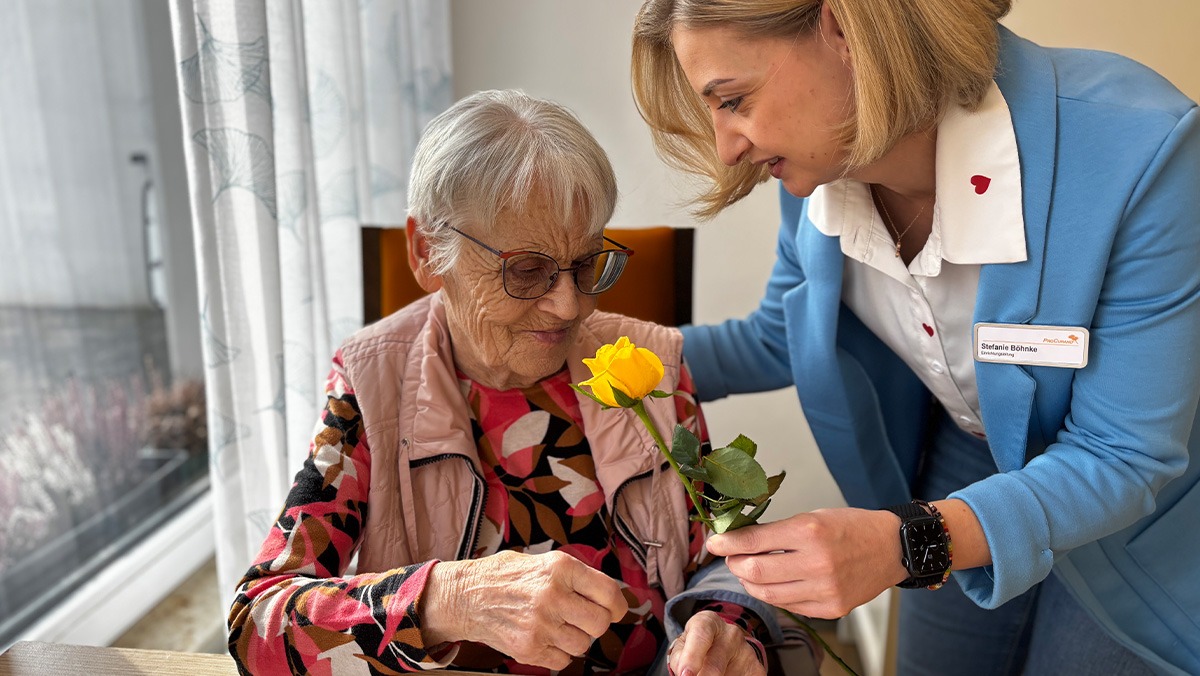 Seniorin und Pflegedienstleitung der Seniorenresidenz Bölschestraße Pflegedienstleitung der Seniorenresidenz Bölschestraße überreicht einer Seniorin eine Rose zum Frauentag